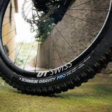 Close-up of a bicycle wheel with 'DT Swiss' and 'Schwalbe Gravity Pro' branding on a blurred natural background.
